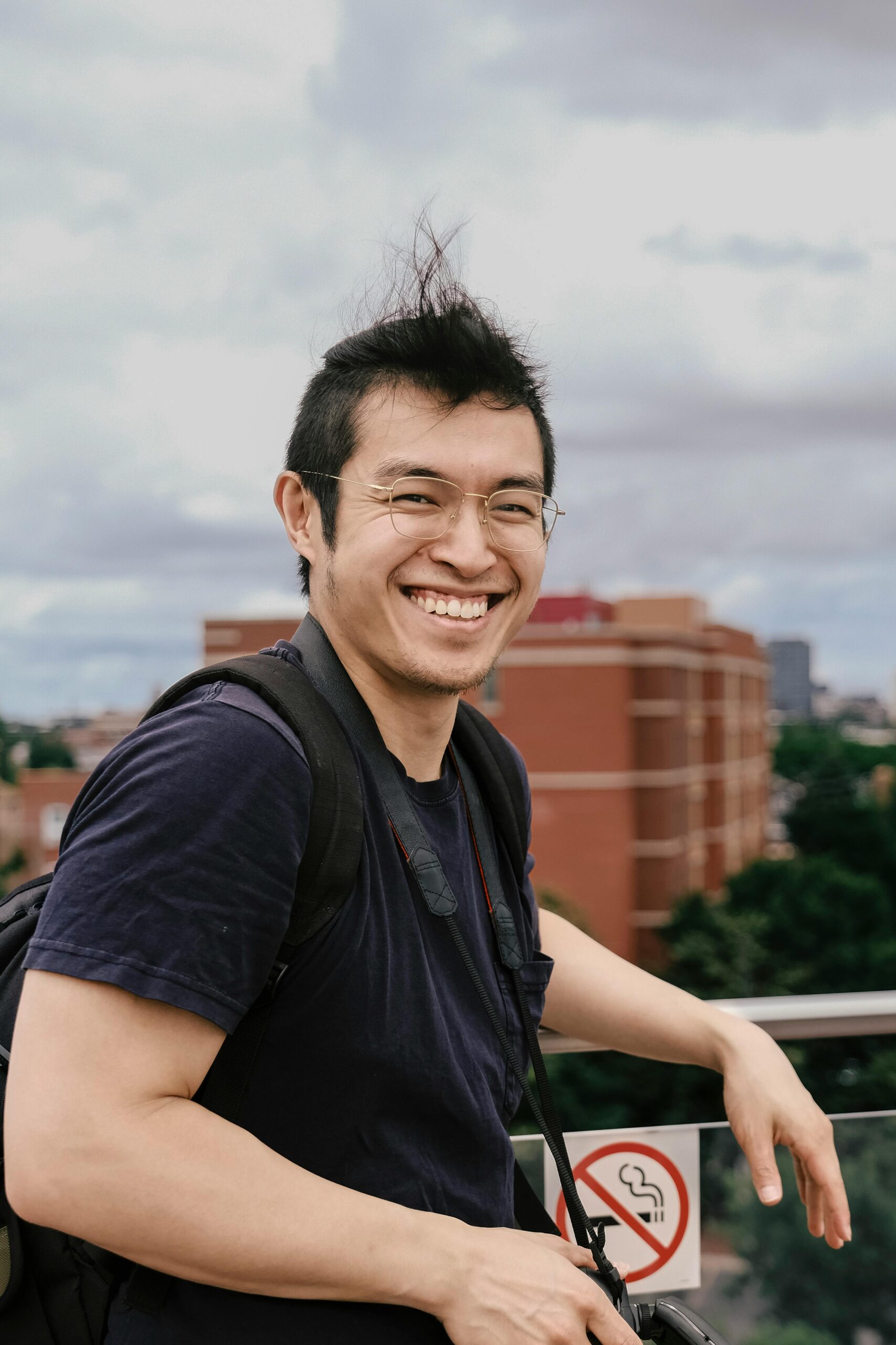 Home A cheerful man smiles while enjoying a cityscape view from a high vantage point on a windy day.